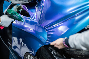 Car wrapping specialist putting vinyl foil or film on car. Selective focus.