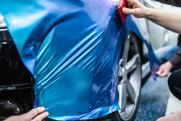 Car wrapping specialist putting vinyl foil or film on car. Selective focus. - obrazy, fototapety, plakaty