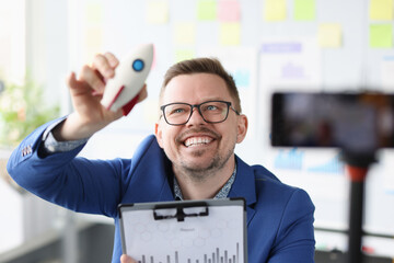 Smiling businessman holding rocket in his hands in front of mobile phone camera