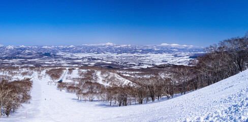 Looking at snowy slopes and view behind from ski resort on a clear day in early spring (Niseko Hanazono Resort, Hokkaido, Japan)