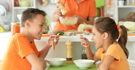 Cute brother and sister tasting salad together in kitchen