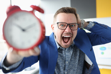 Young man holding alarm clock and shouting