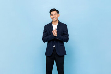 Smiling young handsome southeast Asian man clapping hands impressively in light blue studio...