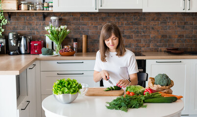 Brunette Woman in white t-shirt preparing vegetable salad in the kitchen at home, Wife Cutting ingredients on table. Healthy Food, Vegan Salad. Dieting Concept.