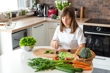 Brunette Woman in white t-shirt preparing vegetable salad in the loft kitchen at home, Wife Cutting ingredients on table. Healthy Food, Vegan Salad. Dieting Concept.