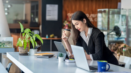 Asian businesswoman working using tablet holding coffee in the office.