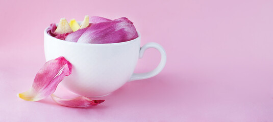 Obraz na płótnie Canvas white cup full of fresh flowers petals of tulips on a pink background. banner