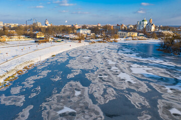 Nice top view of the winter city. Houses and buildings in the snow. Bridge over river. Orthodox churches and a Catholic cathedral. The river is covered with ice.