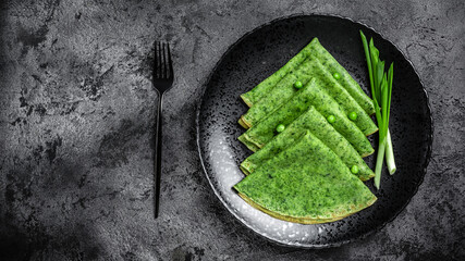 Green vegan crepes with spinach on dark background. Healthy breakfast, vegetarian food, banner, menu recipe place for text, top view