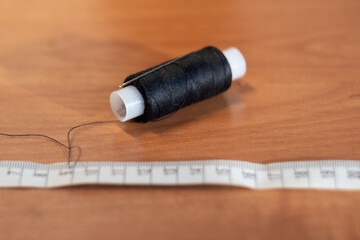 a spool of black thread and a needle lie on a wooden table