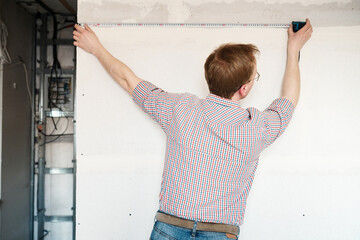 Builder measures the wall with a tape measure