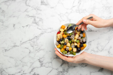 Woman with delicious exotic fruit salad at white marble table, top view. Space for text