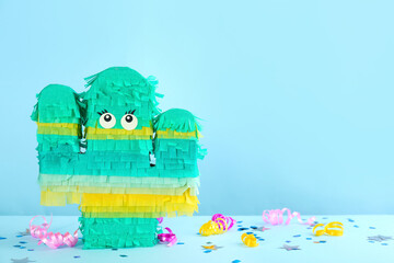 Cactus shaped pinata and decor on light blue background. Space for text
