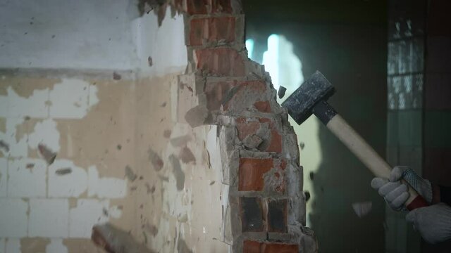 A worker with a sledgehammer demolishes a brick wall. The concept of overcoming obstacles in life and work.