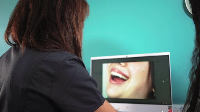 Woman professional dentist discusses treatment plan with patient at computer with photos of teeth and jaw. Processes in a dental clinic. Dentistry. Concept medicine and healthcare.