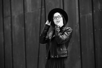 Beautiful russian girl dressed in black leather clothes and eyeglasses. Rock style european woman in urban background.