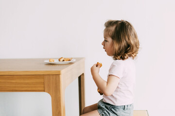 A little girl sits at a table and eats cookies