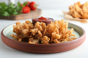 Delicious onion blossom with ketchup served on white wooden table, closeup