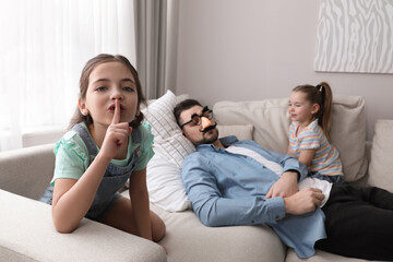 Cute little children putting funny glasses on father while he sleeping at home