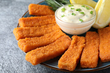 Fresh breaded fish fingers, sauce and lemon served on grey table, closeup