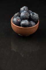 Aerial view of blueberries in bowl, selective focus, on black slate with reflection, vertical, with copy space