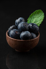 Top view of small bowl with blueberries and mint leaf, on black slate with reflection, in vertical, with copy space