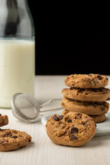 Close-up of chocolate cookies in white plate and bottle with milk, on white table, black background, vertical, with copy space