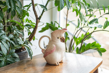 Vintage cockatoo bird kettle - on a wooden table with plants before the window