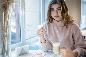 Pretty young woman sitting in the cafe with a cup of cappuccino and looking at the camera.