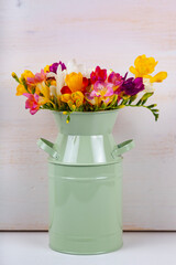 Freesia in a vase on a wooden background.