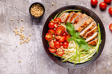 Fried chicken fillet and fresh vegetable salad of tomatoes, zucchini and pine nuts.
