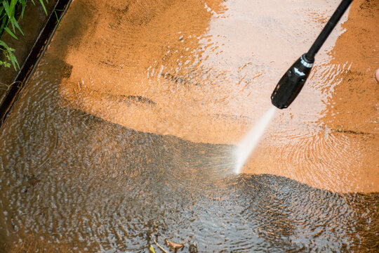 Selective focus. Cleaning backyard paving tiles with high pressure washer.