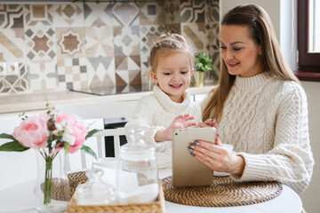 Smiling mother takes selfie with cute daughter on tablet, happy young mom laughing makes photo with daughter at home, single mom and adopted children playing fun with phone