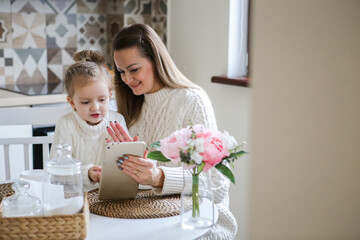 Obraz na płótnie Canvas miling mother takes selfie with cute daughter on tablet, happy young mom laughing makes photo with daughter at home, single mom and adopted children playing fun with phone