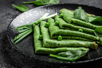 Rolled thin green colored pancake with spinach and vegetables on top. Food recipe background. Close up