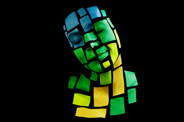 Portrait of a young woman with bold glowing makeup posing in the studio. Shape of green, yellow, blue colored squares on woman face. Isolated on black background.