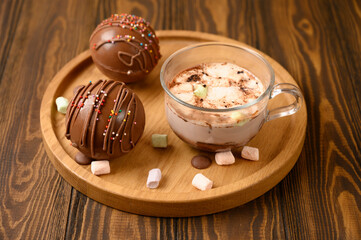 Cocoa bomb that melts with hot milk. Cup of dark hot chocolate. Comfort food. White wood table with...