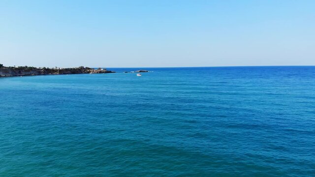 Beautiful green-blue colour of calm Aegean sea, aerial shot. Rocky cape land seen ahead, small tourist boat sail towards. Mellow season time at north shore of Crete Island