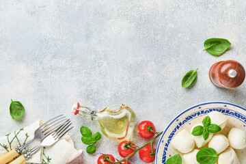 Mozzarella cheese with basil in white ceramic plate, tomato cherry olive oil and spice grinder, condiments, pepper tomato cherry on slate stone background. Mock up. Ingredients for Caprese salad.