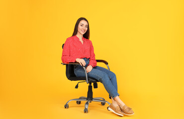 Young woman sitting in comfortable office chair on yellow background