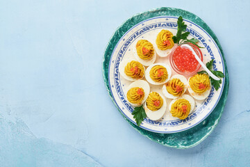 Stuffed eggs with red caviar and paprika on blue plate for appetizer easter table, top view, copy space. Traditional dish for Happy Easter holiday.