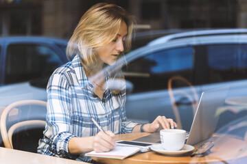 Young blond woman using laptop at cafe, she working on laptop computer at coffee shop. Freelance work. Online courses.