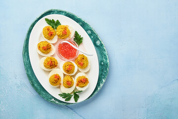 Stuffed eggs with red caviar and paprika on blue plate for appetizer easter table, top view, copy space. Traditional dish for Happy Easter holiday.