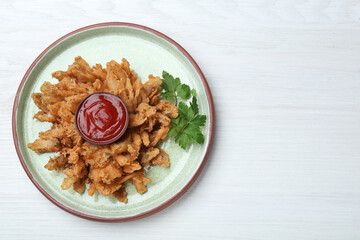 Delicious onion blossom with ketchup served on white wooden table, top view. Space for text