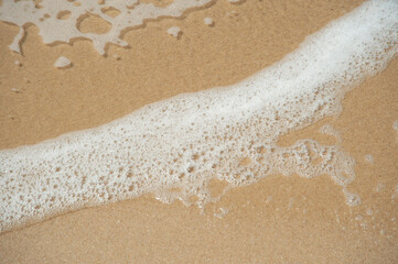Fototapeta na wymiar Soft sea wave with sea foam on sandy beach.