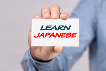 a man's hand holds a card with the inscription LEARN JAPANESE