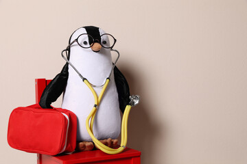 Toy penguin with eyeglasses, stethoscope and first aid bag on beige background, space for text. Pediatrician practice © New Africa