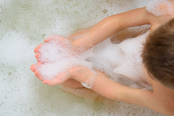 The child is bathing in the bathtub. Foam on hands while bathing. Cleanliness is the key to health. All children really like foam and soap bubbles.