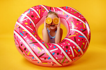 Summer concept. Little girl with halves of an orange lying on an inflatable donut circle. Child in...