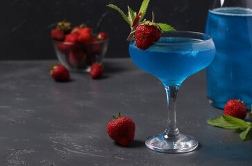Shimmering blue champagne in glass with garnish strawberry on dark gray background and bottle champagne.